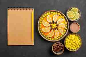 Free photo top view cake with citrus fruits appetizing cake with chocolate and citrus fruits next to the notebook and pencil bowls of slices of lime chocolate and chocolate cream on the black table