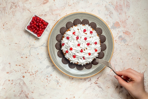 Top view cake with pastry cream and chocolate berries in bowl fork in female hand