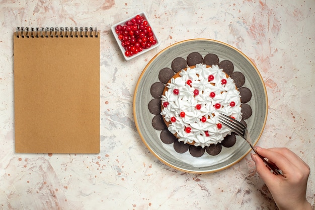 Top view cake with pastry cream and chocolate berry in bowl fork in female hand notebook