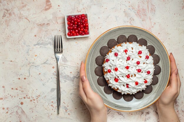 ボウルフォークの女性の手のベリーのペストリークリームとチョコレートのトップビューケーキ