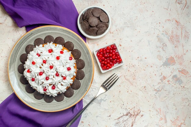 Top view cake with pastry cream and chocolate on plate purple shawl bowls with chocolate and berries fork