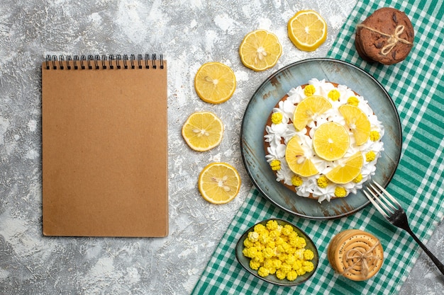 Top view cake with pastry cream and lemon fork on platter cookies candies in bowl on green white checkered tablecloth. empty notebook