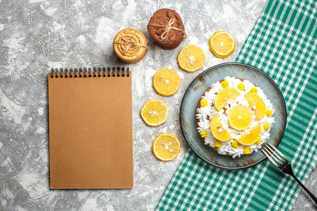 Top view cake with pastry cream and lemon fork on platter on green white checkered tablecloth. empty notebook