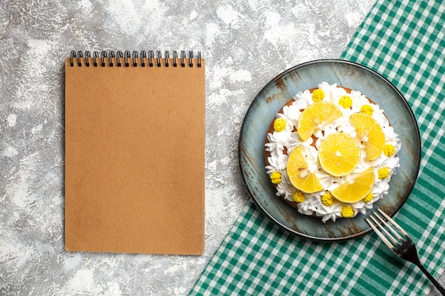 Top view cake with pastry cream and lemon on plate a fork on green white checkered tablecloth. empty notebook