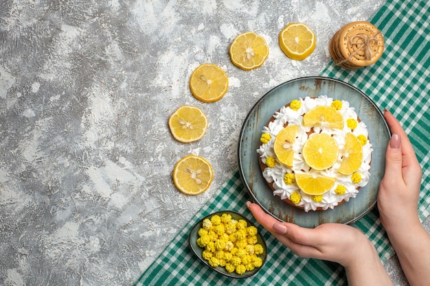 Foto gratuita torta vista dall'alto con crema pasticcera e limone su piatto in mano femminile biscotti caramelle in ciotola su tovaglia a scacchi bianca verde