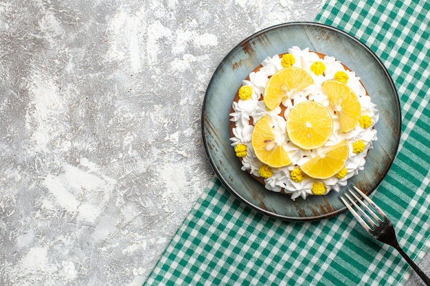 Top view cake with pastry cream and lemon on round plate fork on green white checkered tablecloth