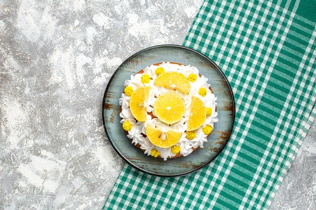 Торт с кондитерским кремом и дольками лимона на круглой тарелке на зелено-белой клетчатой скатерти, вид сверху