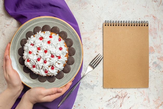 Foto gratuita torta vista dall'alto con crema pasticcera sul piatto in quaderno con forchetta a scialle viola a mano femminile