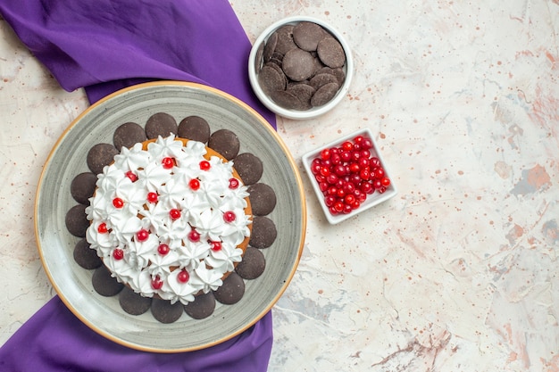 Вид сверху торт с кондитерским кремом на тарелке фиолетовые шалевые миски с шоколадом и ягодами на сером столе
