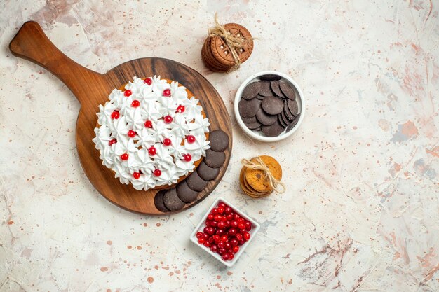 ロープで結ばれたベリーとチョコレートクッキーとまな板ボウルに白いペストリークリームとチョコレートのトップビューケーキ