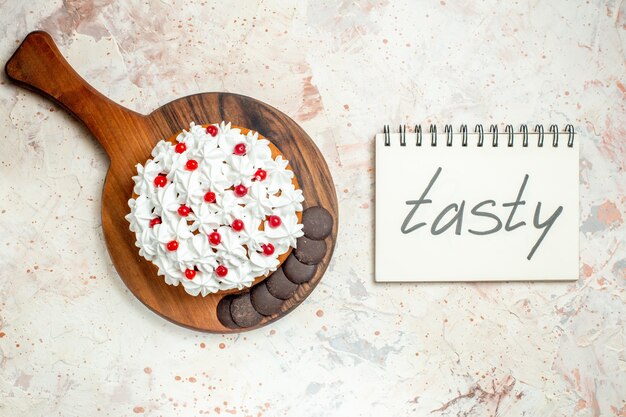 top view cake with white pastry cream and chocolate on wooden cutting board tasty written on notebook