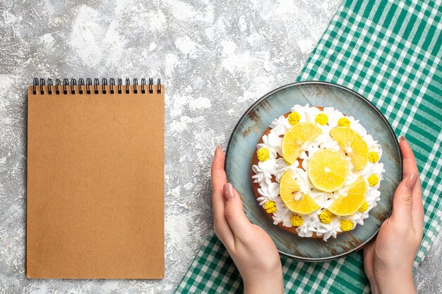 Top view cake with white pastry cream and lemon slices on cyan plate on green and white checkered tablecloth