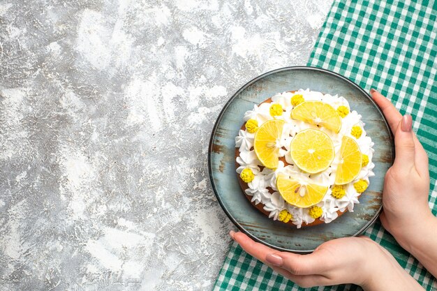 Top view cake with white pastry cream and lemon slices on round plate in female hand