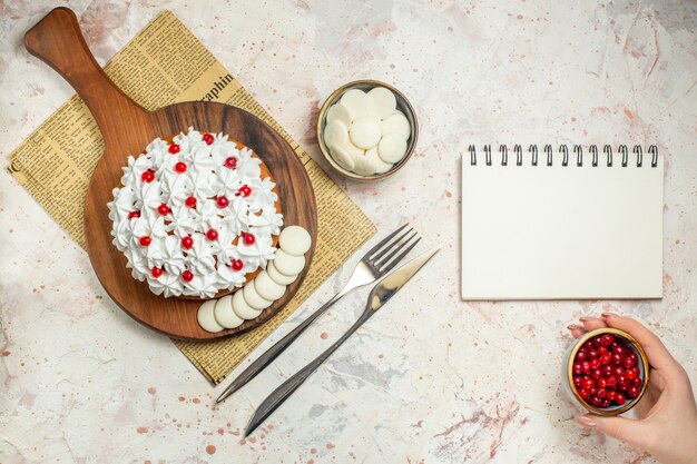 신문에 나무 보드에 흰색 과자 크림과 함께 상위 뷰 케이크. 여자 손에 딸기와 그릇. 빈 노트