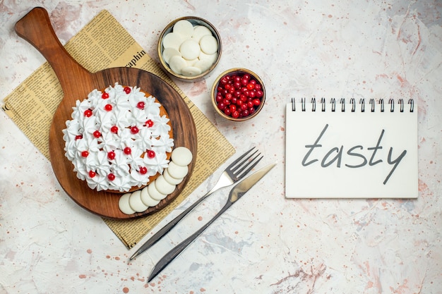 Top view cake with white pastry cream on wood board on newspaper . tasty written on notebook