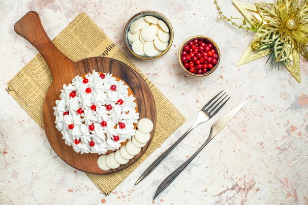 Вид сверху торт с белым кондитерским кремом на деревянной доске на газете и рождественском орнаменте