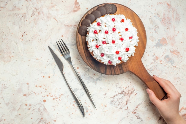 Top view cake with white pastry cream on wooden cutting board in female hand