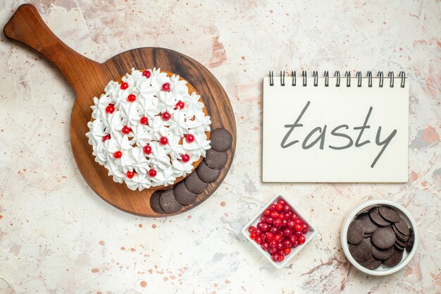 Top view cake with white pastry cream on wooden cutting board tasty written on notebook