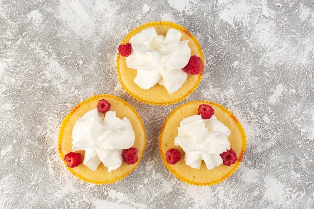 Vista dall'alto torte con crema gustosissima al forno progettate con lampone sulla scrivania grigia zucchero dolce cuocere al forno crema di biscotti