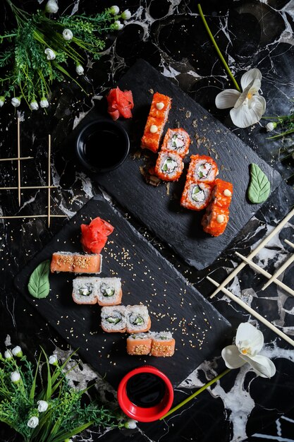 Top view california sushi rolls with philadelphia rolls on stands with soy sauce wasabi and ginger with flowers