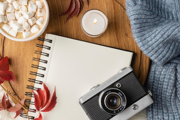 Top view of camera and notebook with cup of hot cocoa with marshmallows