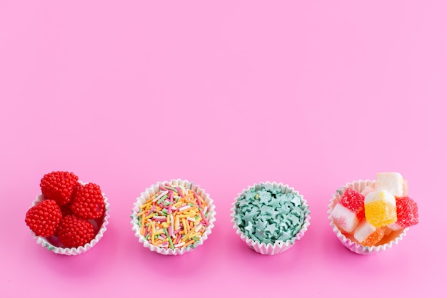 A top view candies and marmalade inside little paper packages on pink