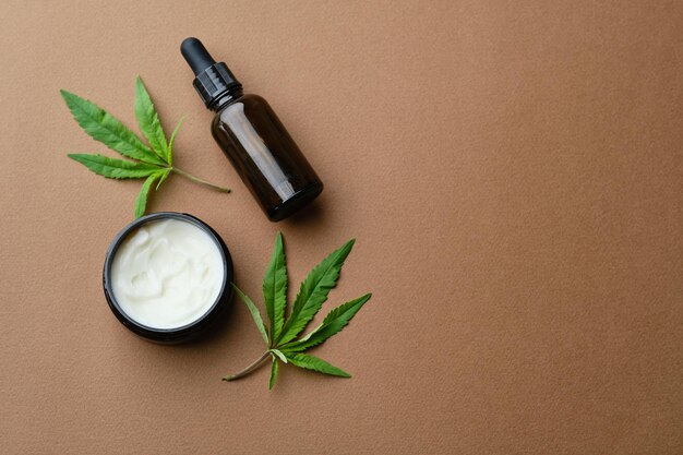 Free photo top view of cannabis cosmetic oil cream in jar bottle and a green plant leaf natural cosmetic on brown background flat lay copy space