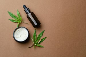 Top view of cannabis cosmetic oil cream in jar bottle and a green plant leaf natural cosmetic on brown background flat lay copy space