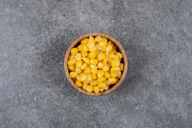 Top view of canned sweet corns in wooden bowl over grey table.