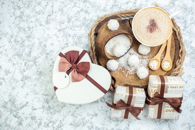 Foto gratuita vista dall'alto tazza cappuccino polvere di cocco ciotola cucchiai di legno su tavola di legno regali a forma di cuore confezione regalo su superficie grigia