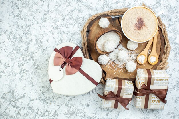 Top view cappuccino cup coconut powder bowl wooden spoons on wood board gifts heart shaped giftbox on grey surface