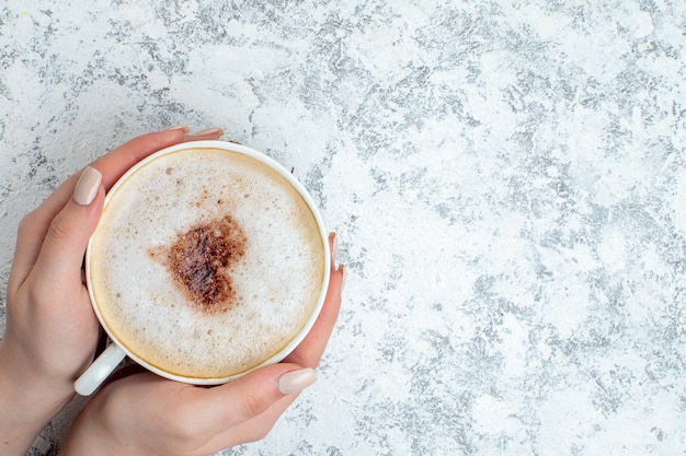 Top view cappuccino cup in female hand on grey surface with copy place