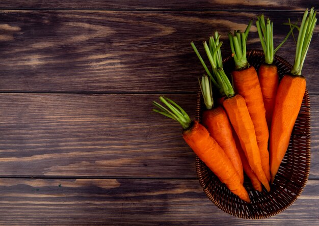 top view of carrots in basket on wooden background with copy space
