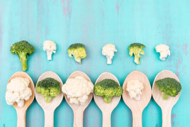 Top view cauliflower and broccoli in wooden spoon on blue surface