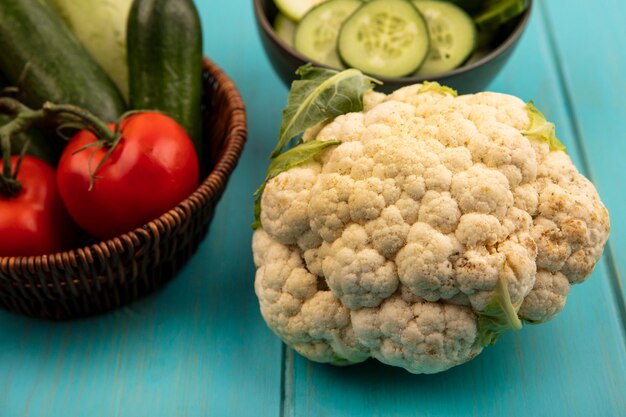 Top view of cauliflower with fresh vegetables such as tomatoes and cucumbers on a bucket on a blue wooden surface