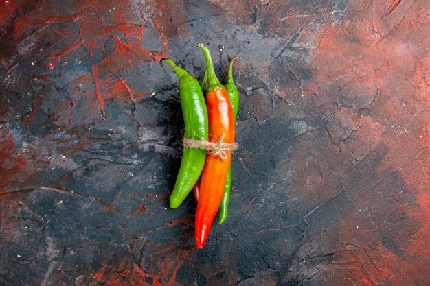 Top view of cayenne peppers in different colors and sizes tied in one another with rope on mixed color background