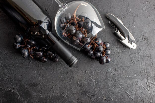 어두운 바닥에 뒤집힌 와인 잔과 와인 병 와인 오프너에 있는 매력적인 검은 포도