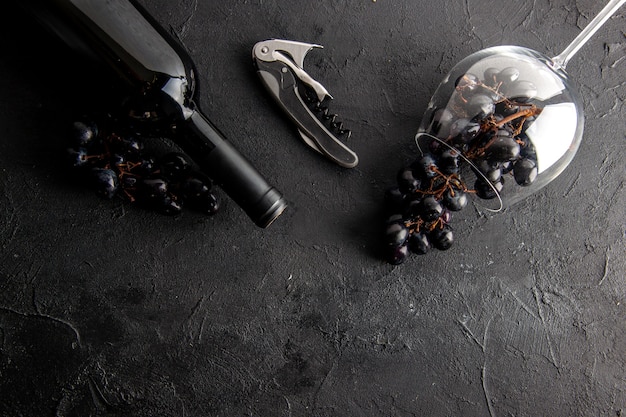 Free photo top view charming grapes in overturned wine glass and wine bottle wine opener on black table