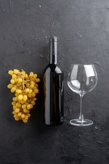 暗い​背景​に​魅力的​な​黄色​ブドウ​の​ワイン​ボトル​と​ガラスワインオープナー​の​上面図