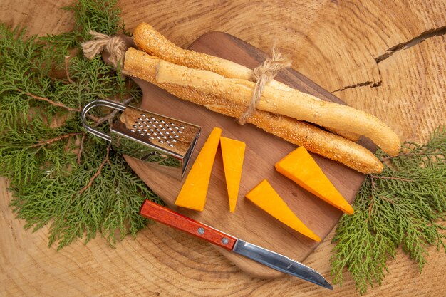 Top view cheese and bread box grater knife on chopping board pine tree branches on wooden table