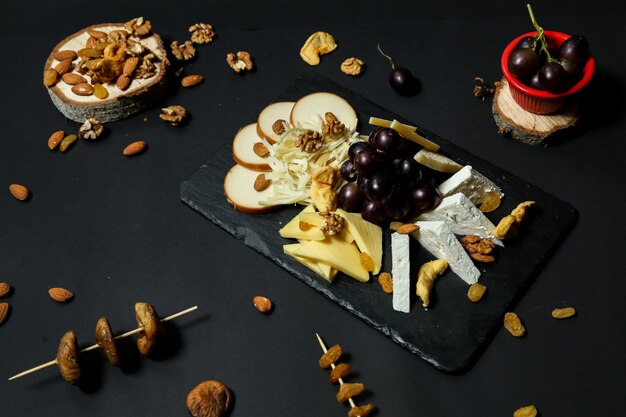 Top view cheese plate with grapes and nuts on a stand with dried fruits on a black table