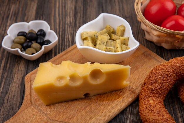 Top view of cheese with slices of cheese on a bowl on a wooden kitchen board with olives on a bowl on a wooden background