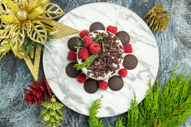 Torta di formaggio di vista superiore con cioccolato e lamponi sugli ornamenti di natale del piatto ovale bianco sulla superficie grigia