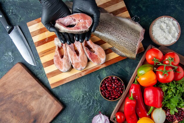 Top view chef holding raw fish slices vegetables on wood serving board on kitchen table