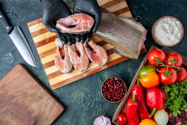 Top view chef holding raw fish slices vegetables on wood serving board on kitchen table