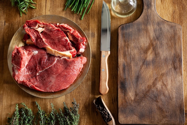 Top view of chef knife next to big chunks of red meat and green vegetables on wooden table. Fresh meat.