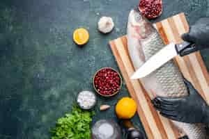 Free photo top view chef with black gloves cutting raw fish on cutting board pepper grinder pomegranate seeds in bowl on kitchen table copy place