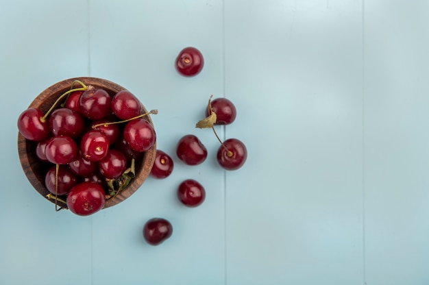 Top view of cherries in bowl and on blue background with copy space