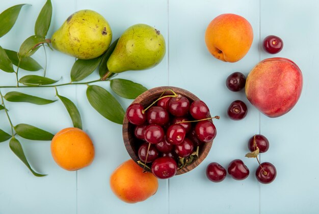 ボウルにさくらんぼと梨のパターンの上面図アプリコット桃のさくらんぼの葉と青い背景
