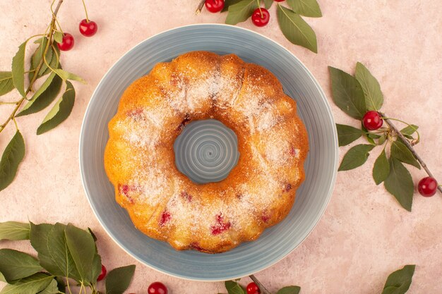 Круглый вишневый торт, вид сверху, сформированный внутри серой тарелки на розовом письменном столе, печенье, сладкое